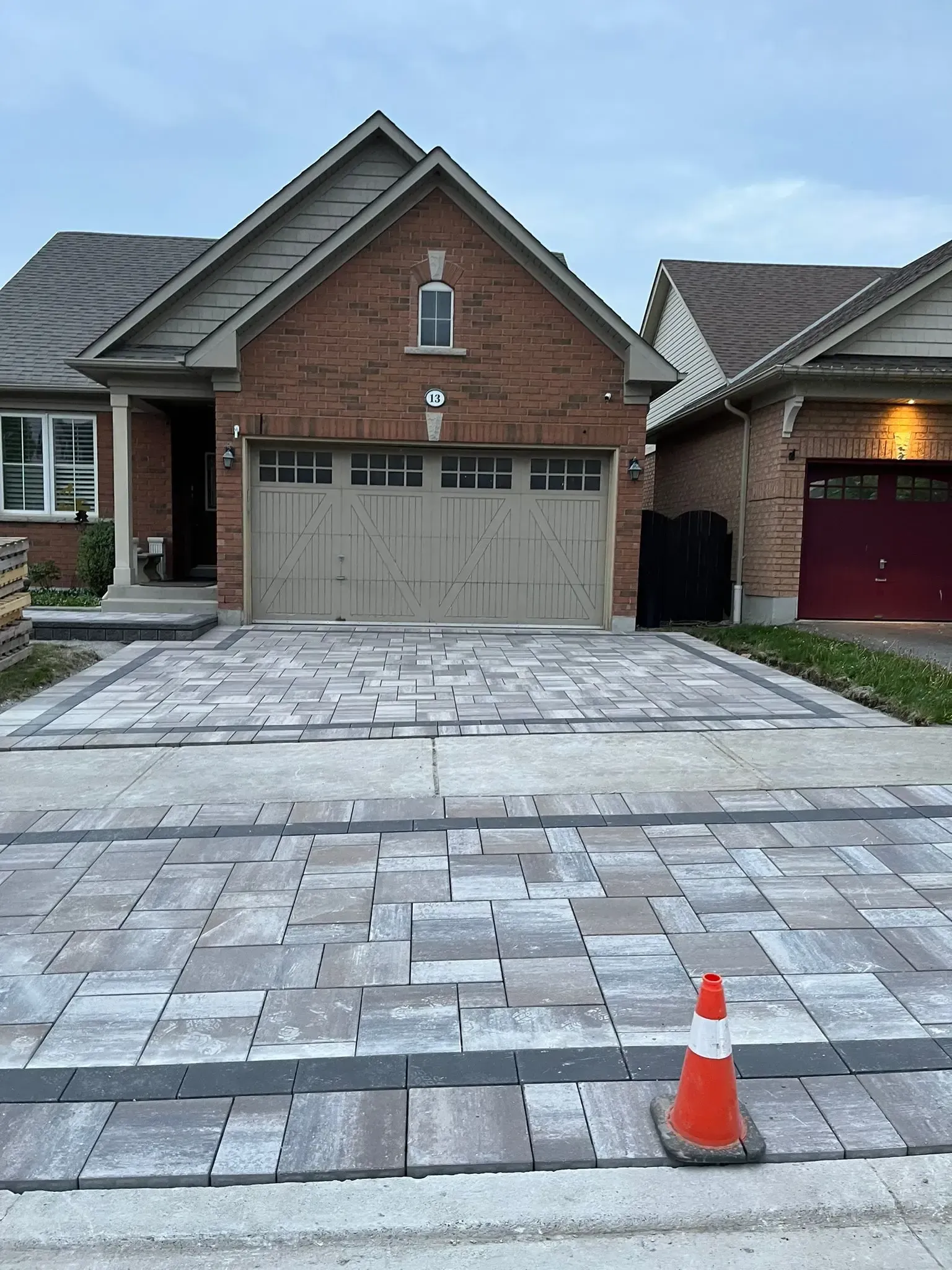 House with brick facade and new gray paving stones in the driveway; orange traffic cone present.