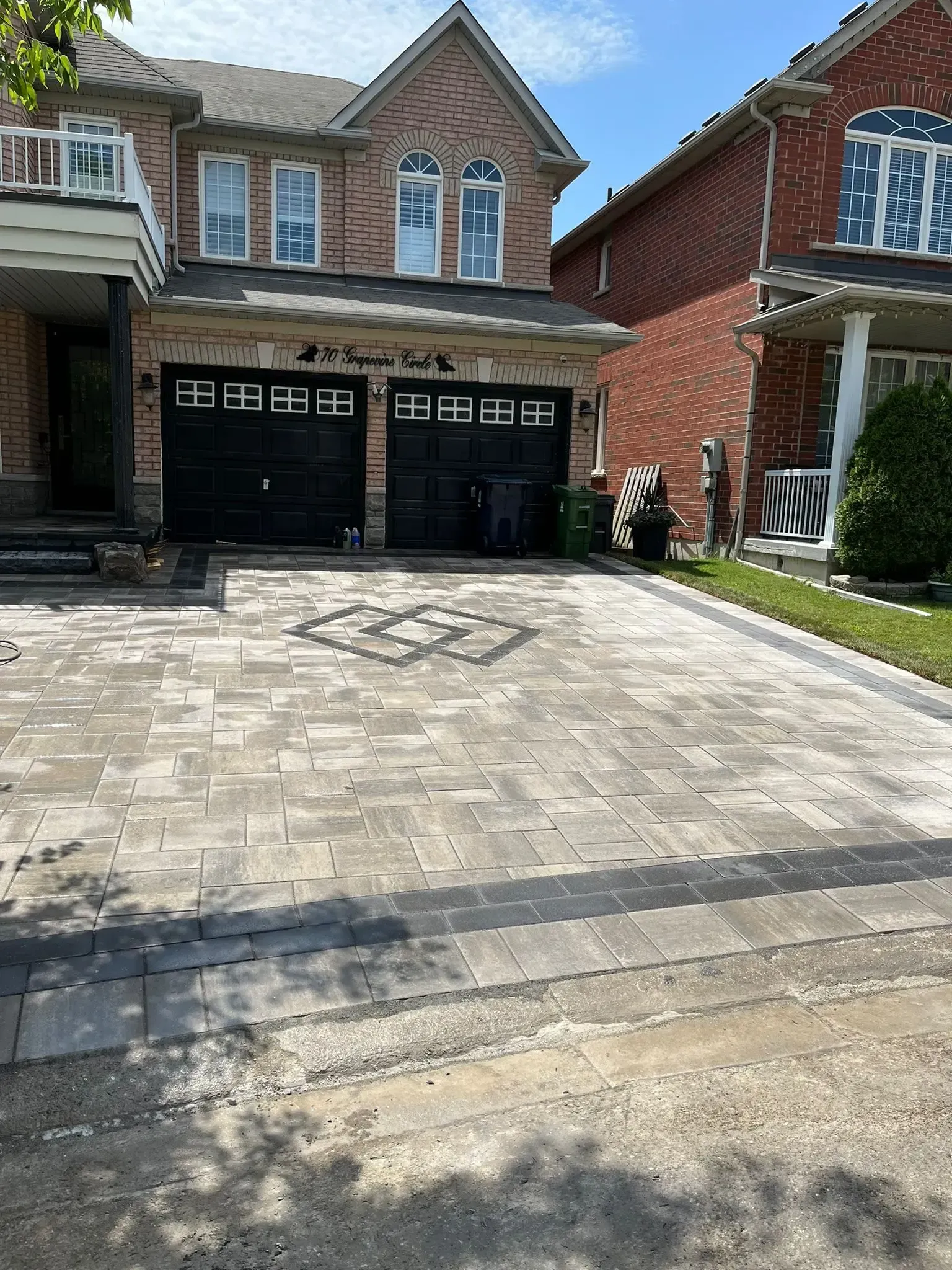 Brick home with paver driveway and two-car garage. Black garage doors and green trash bin visible.