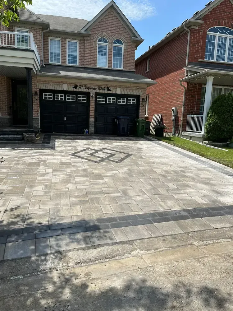 Paver driveway leading to a two-car garage of a brick house; decorative stone pattern in center.