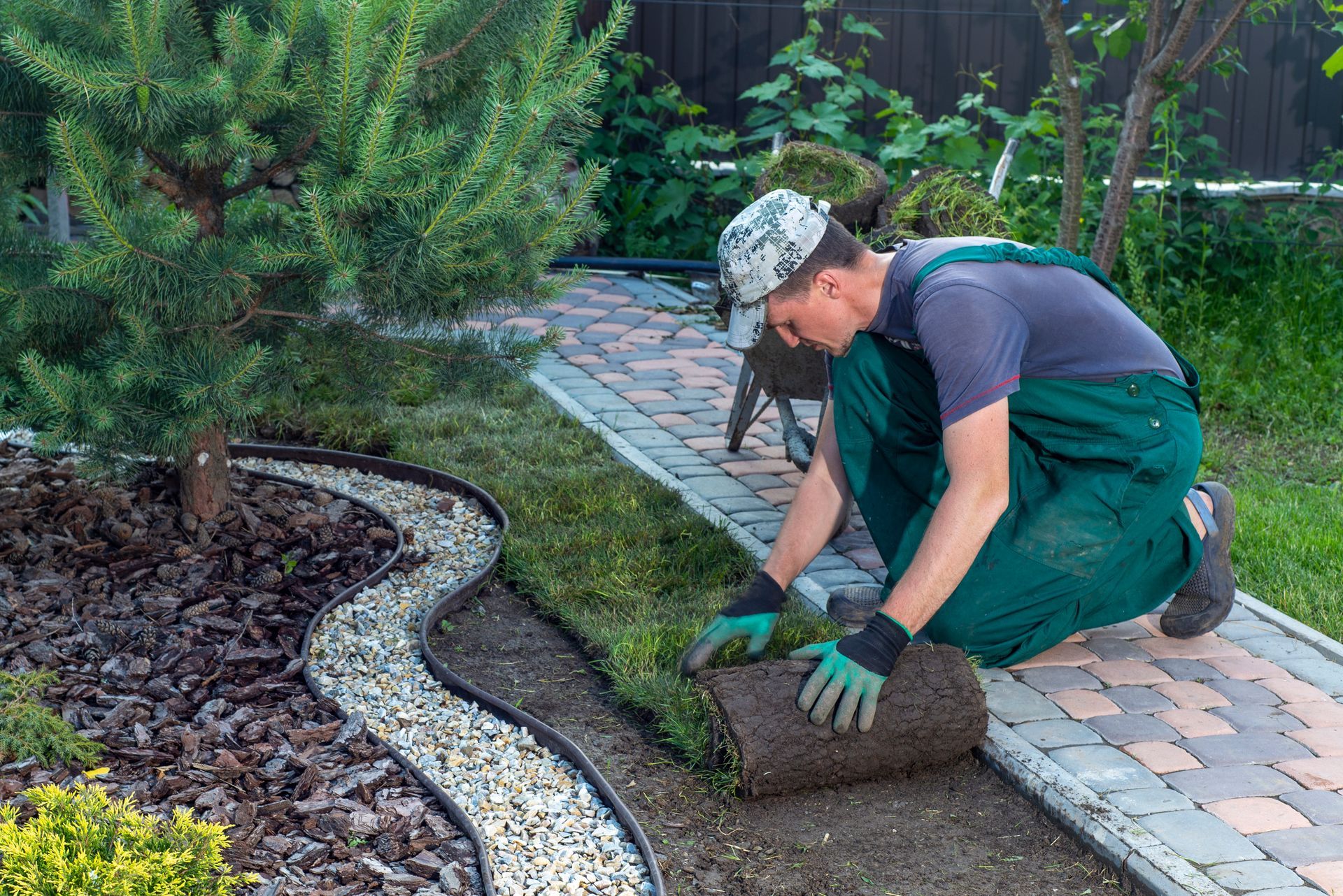 Man rolls out sod along a decorative stone path in a garden.