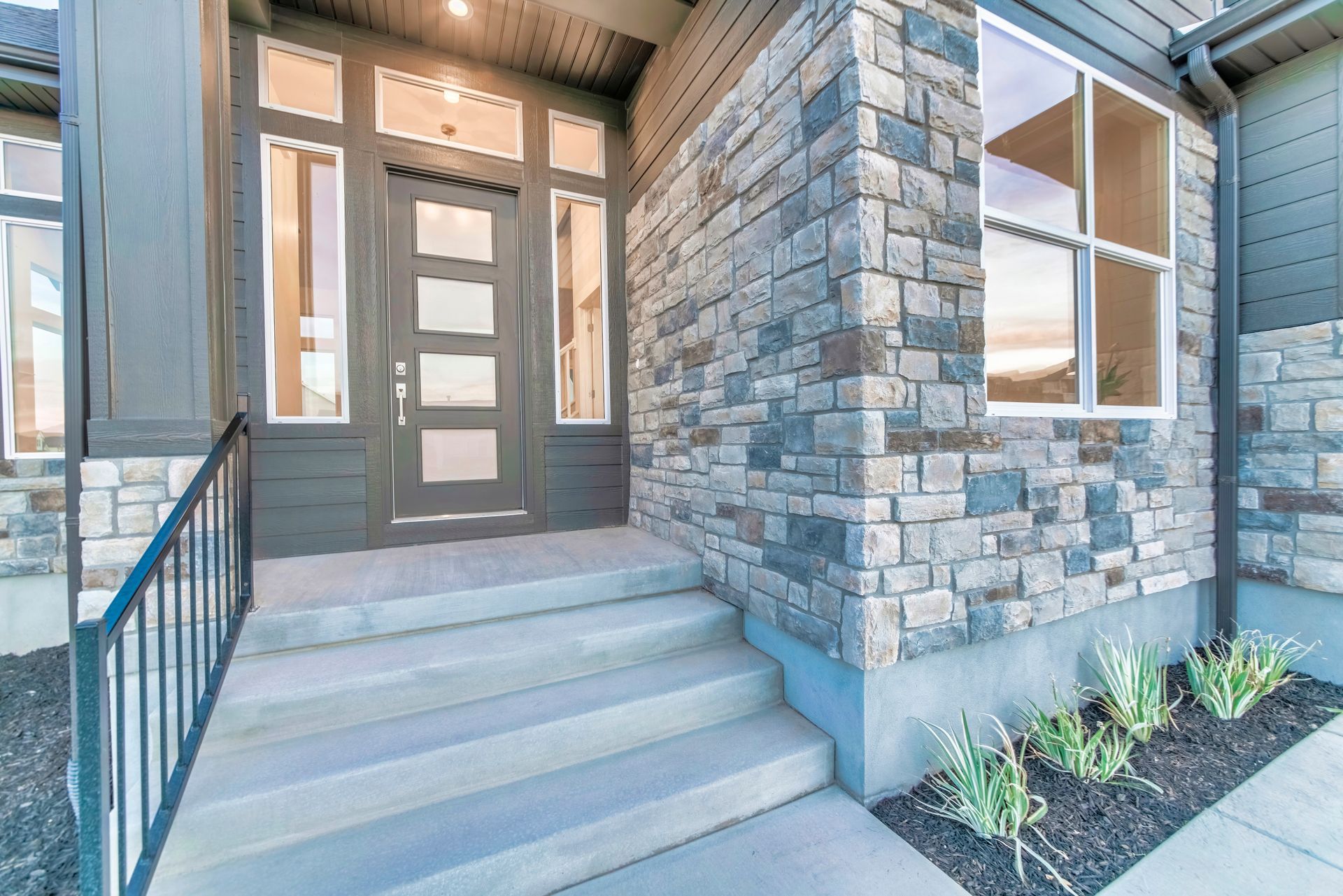 Stone facade entrance with dark door, glass panels, concrete steps, and black railing.