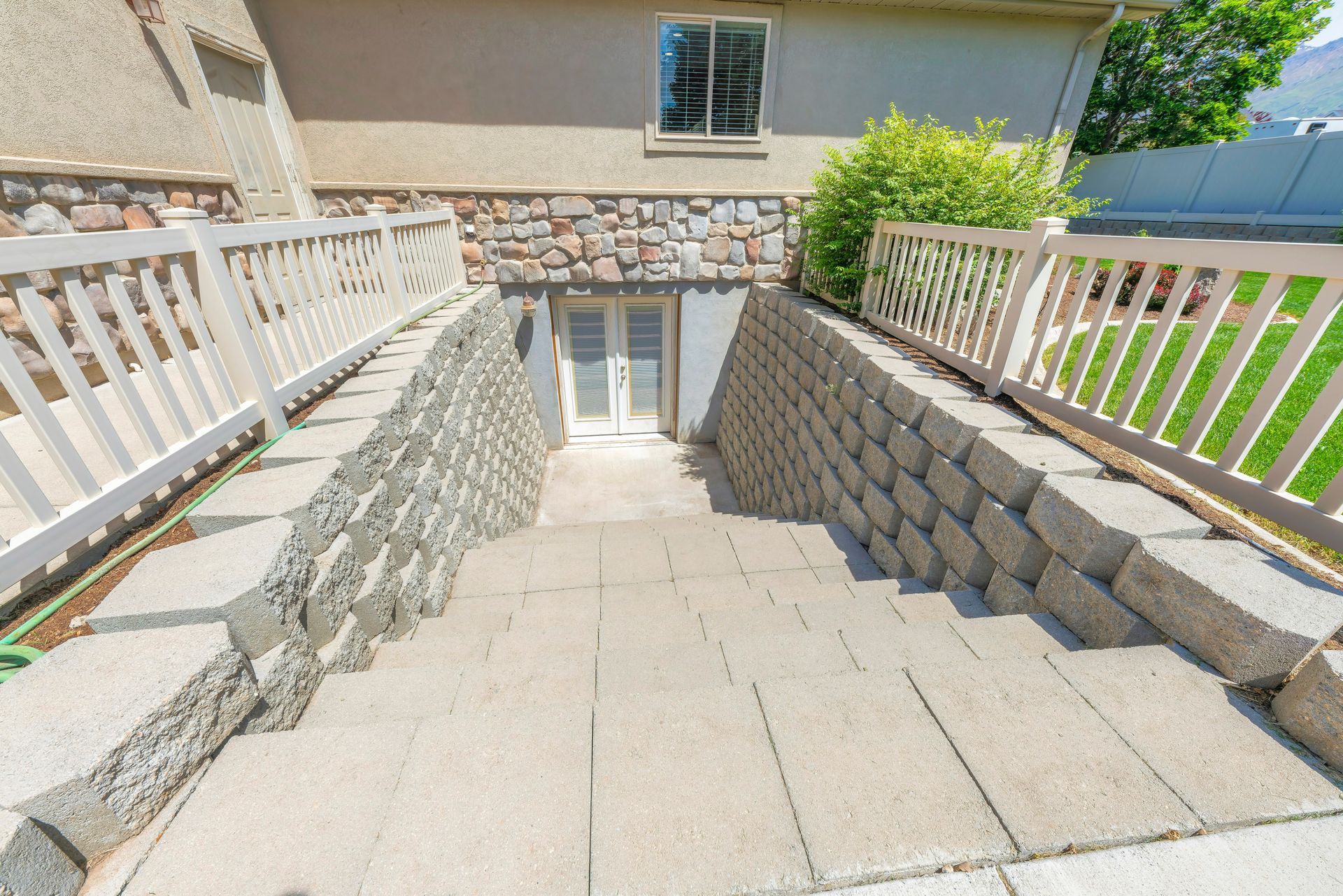 Stone steps leading down to a basement door, flanked by retaining walls and white railings.