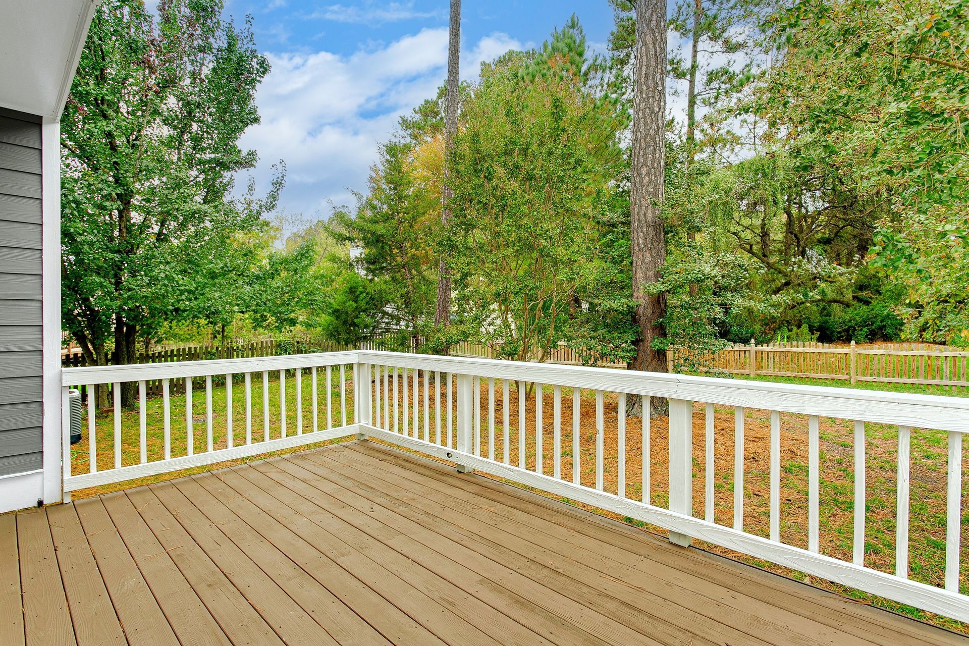 Wooden deck with white railing, overlooking a green yard and trees under a blue sky.
