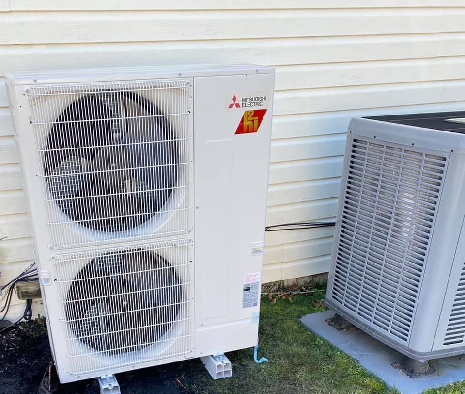 Two air conditioners are sitting outside of a house.