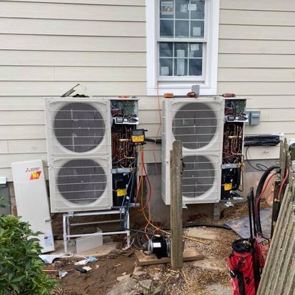 Two air conditioners are being installed on the side of a house.