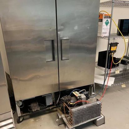 A stainless steel refrigerator is being repaired in a kitchen.
