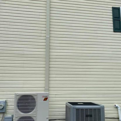 A large air conditioner is sitting on the side of a house next to a window.