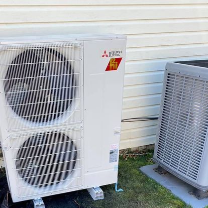 Two air conditioners are sitting next to each other on the side of a house.