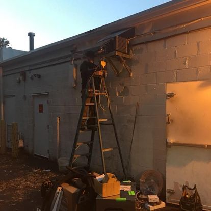 A man is standing on a ladder in front of a brick building.