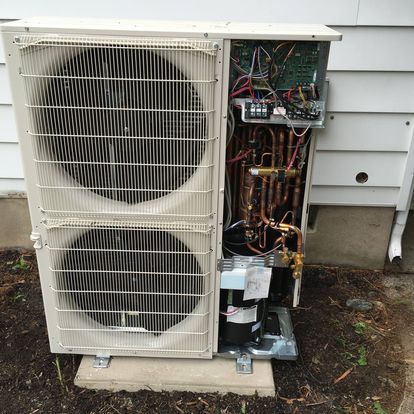 A white air conditioner is sitting on the ground outside of a house.