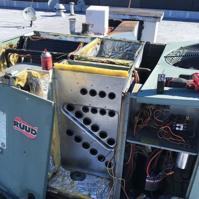 A ruud air conditioner is being repaired on the roof of a building