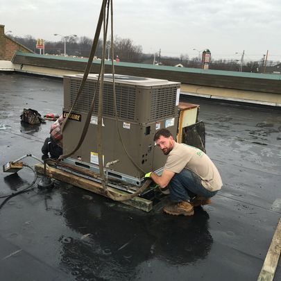 A man is working on an air conditioner on a roof