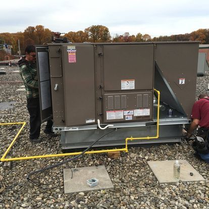 Two men are working on a rooftop air conditioner.