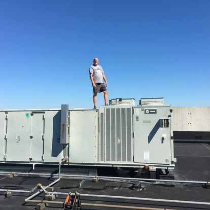 A man standing on top of an air conditioning unit with the word trane on it