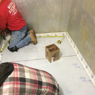 A man in a red shirt is measuring a box on the floor