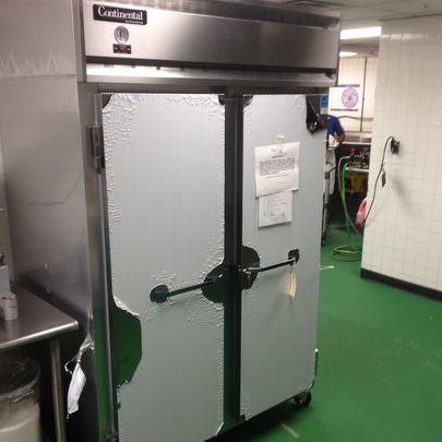 A stainless steel refrigerator is sitting in a kitchen with a green floor.
