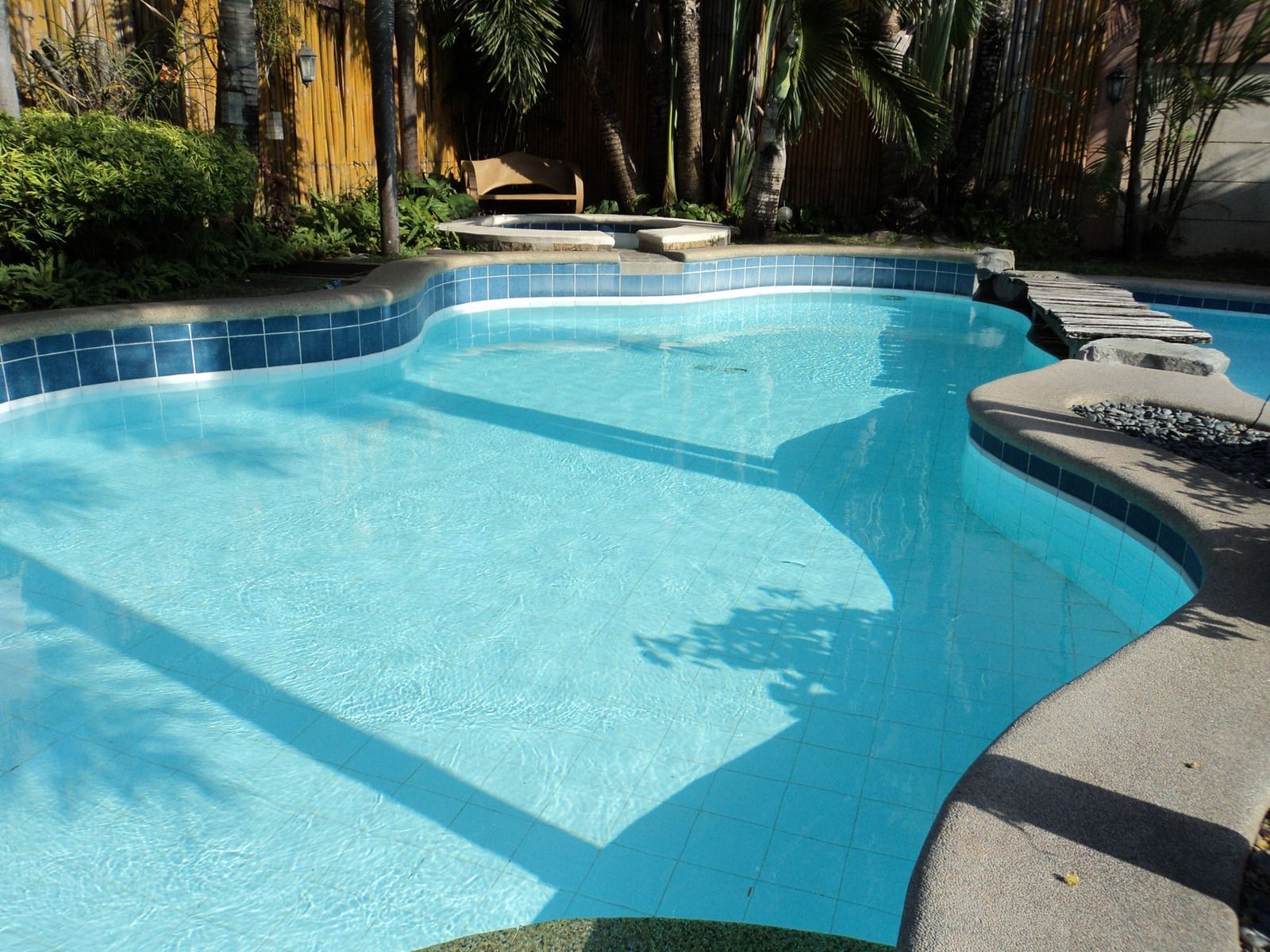 Swimming pool with blue water, surrounded by concrete and greenery.