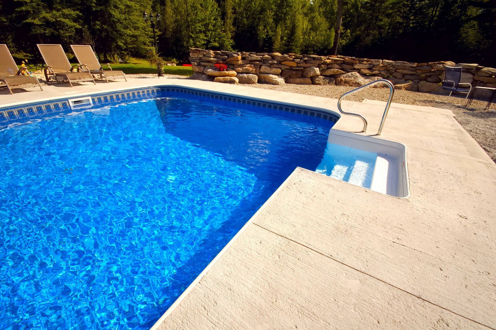 A blue swimming pool with white steps and a concrete deck; lounge chairs on the lawn.