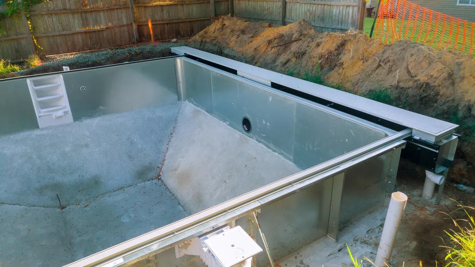 A metal pool under construction, surrounded by dirt and fencing.