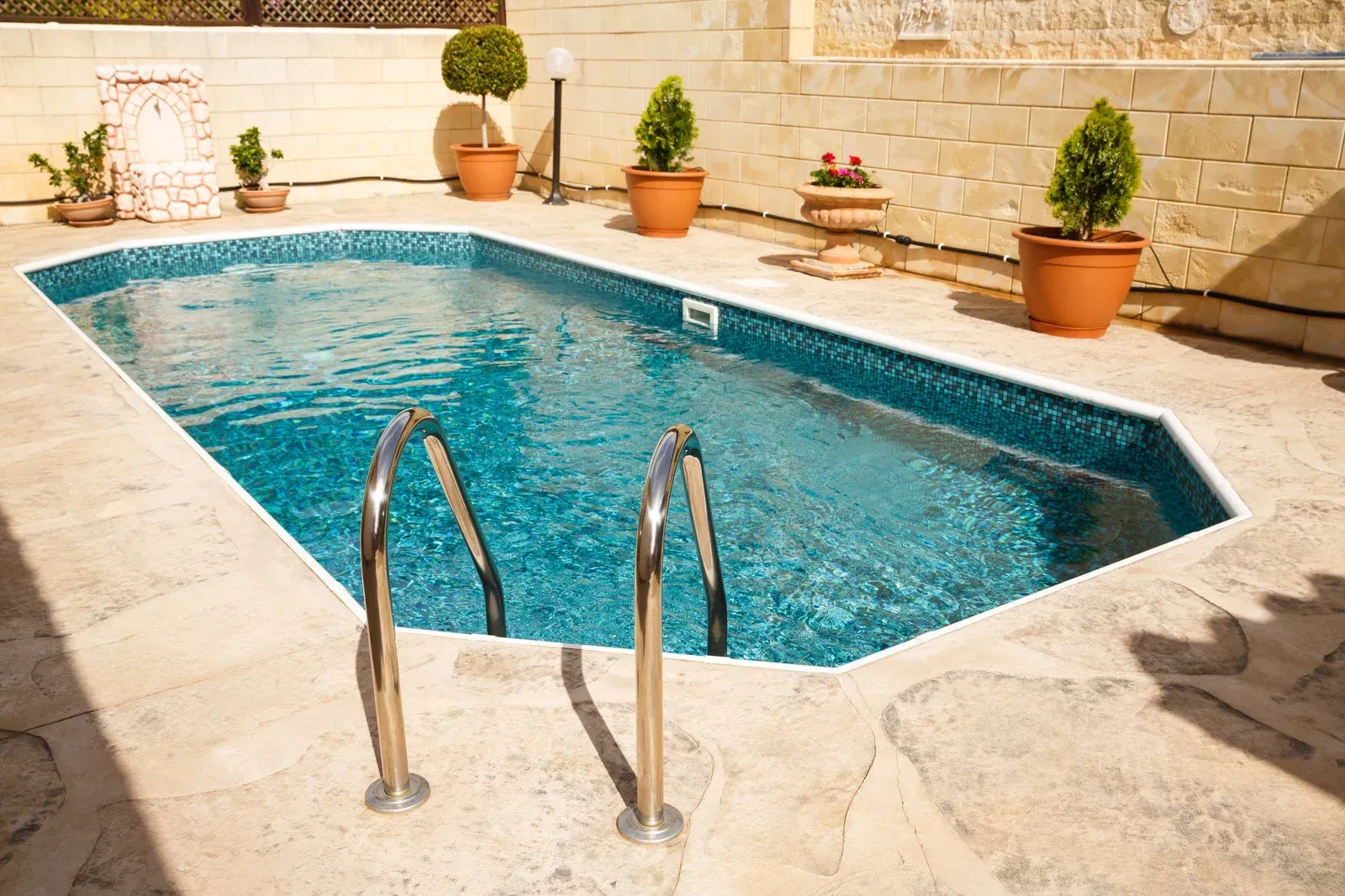 Poolside repair: Tiles removed, piles of dirt, blue pool, blue hose, buckets, and fence in background.