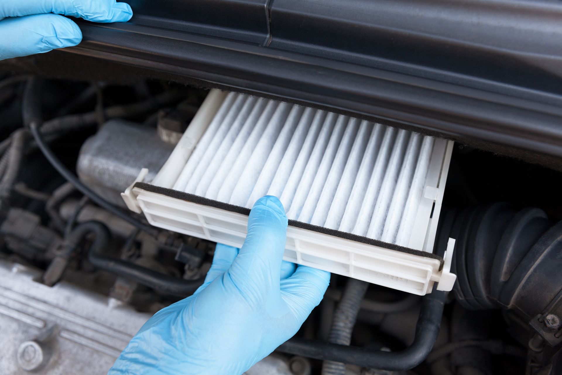 Gloved hands installing a clean white cabin air filter inside a car engine compartment.
