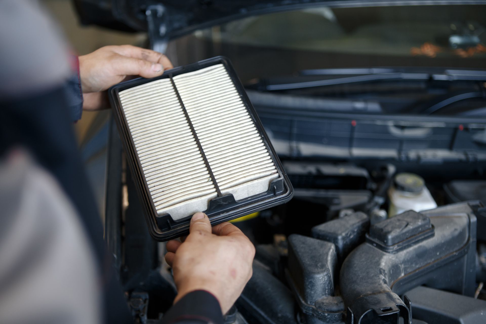 A mechanic holding a clean engine air filter over a car engine bay