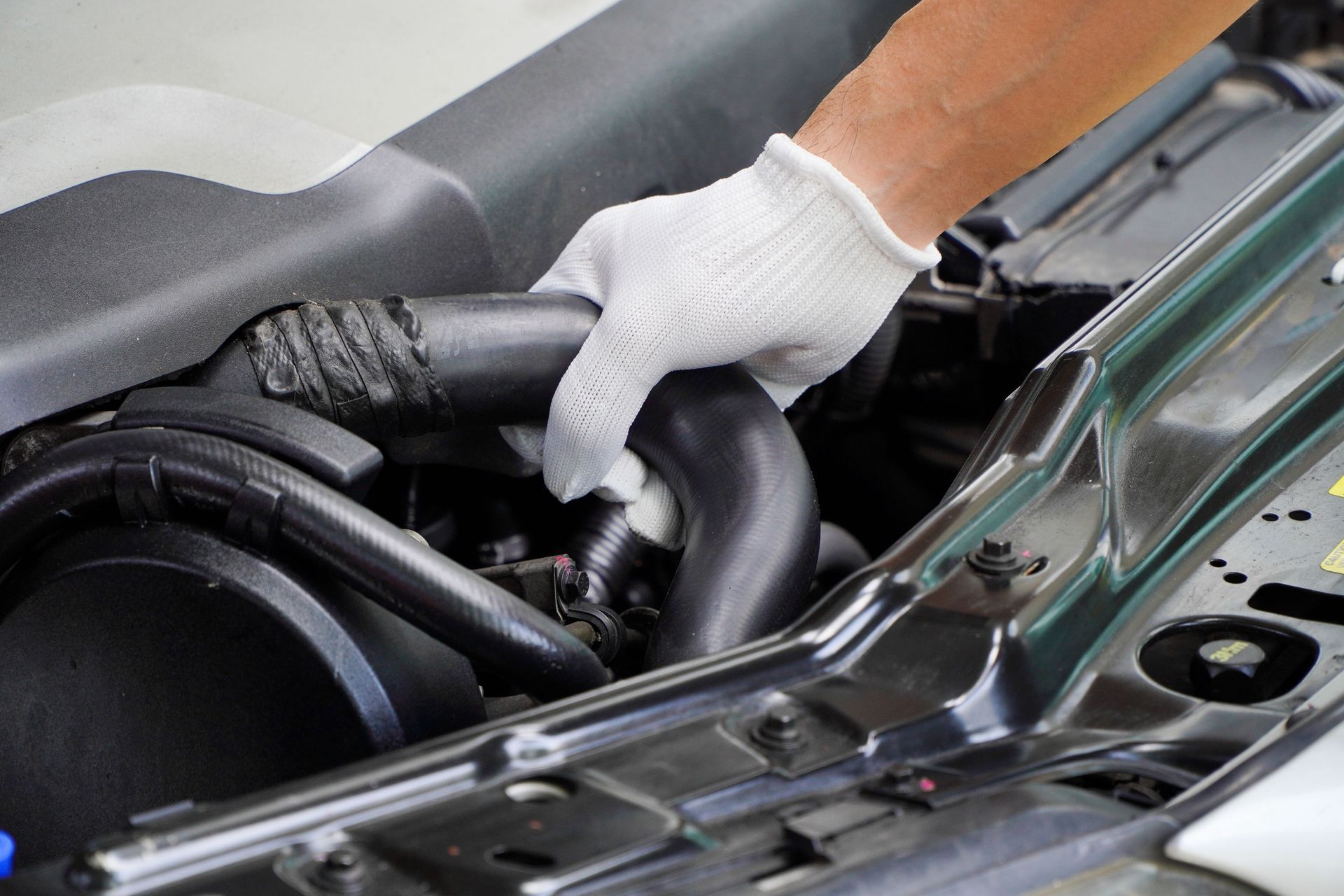 mechanic wearing white gloves checks the radiator hose.