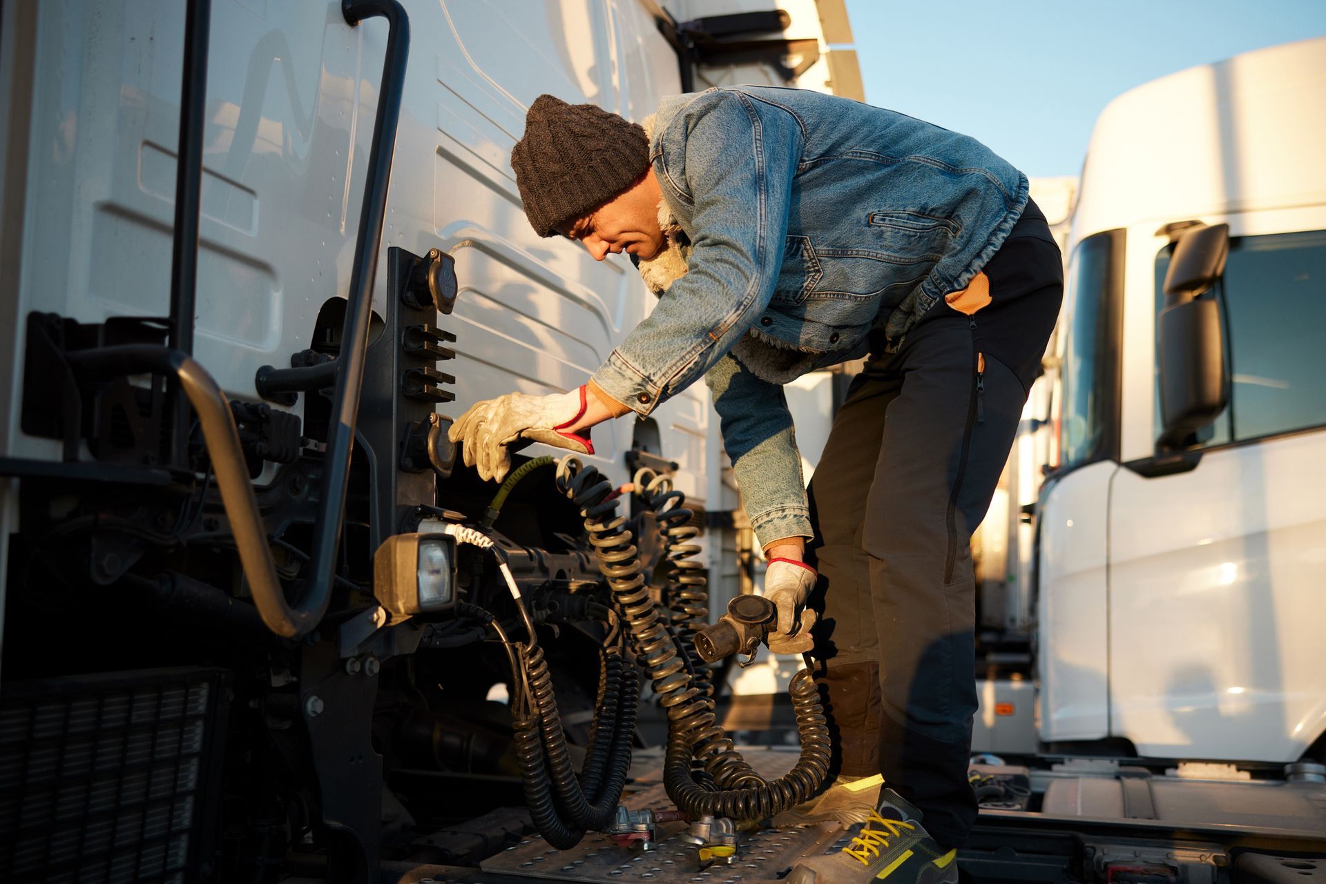 Trucker wearing warm clothes is checking the brake air hose coil.