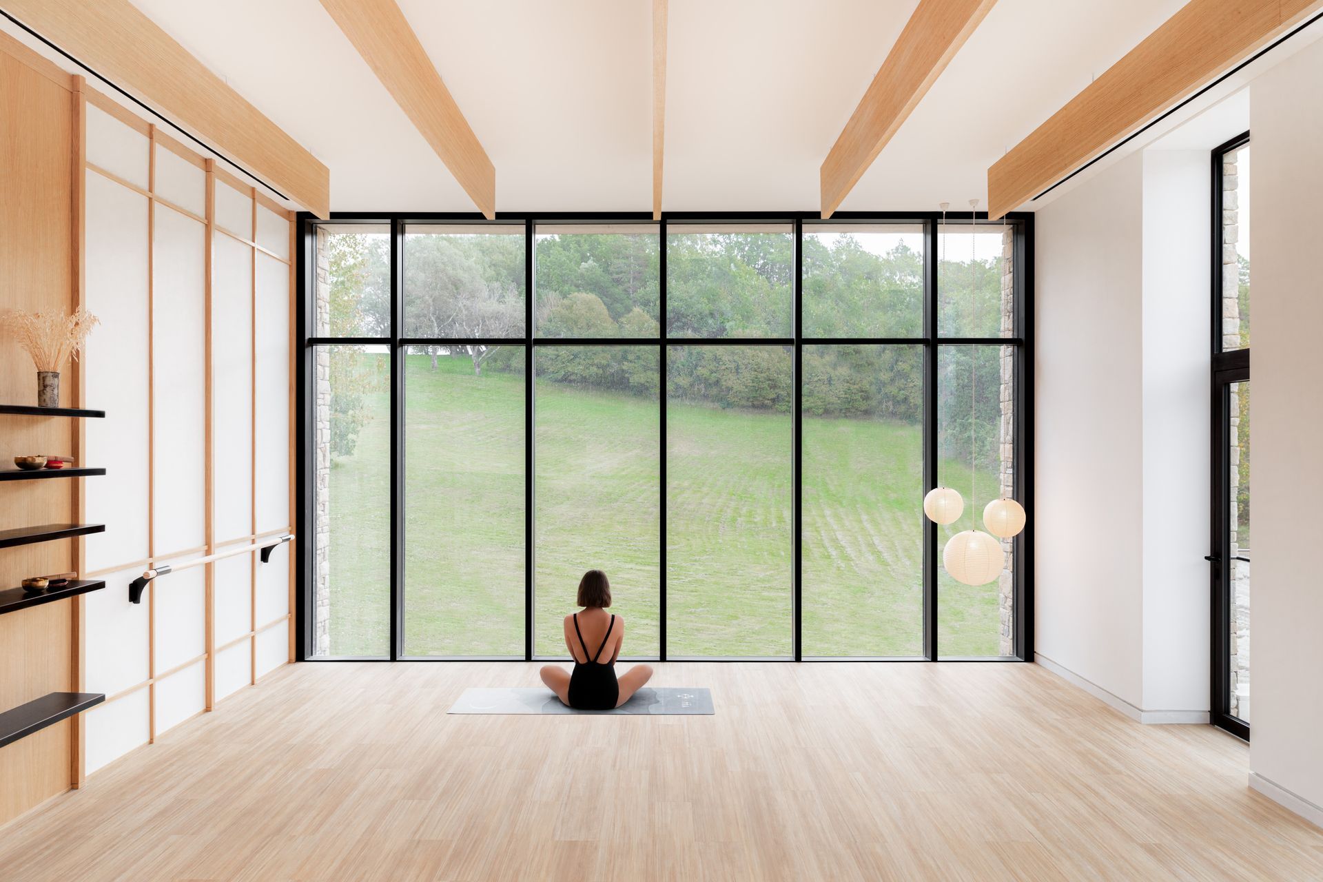 Une femme est assise sur un tapis de yoga devant une grande fenêtre.
