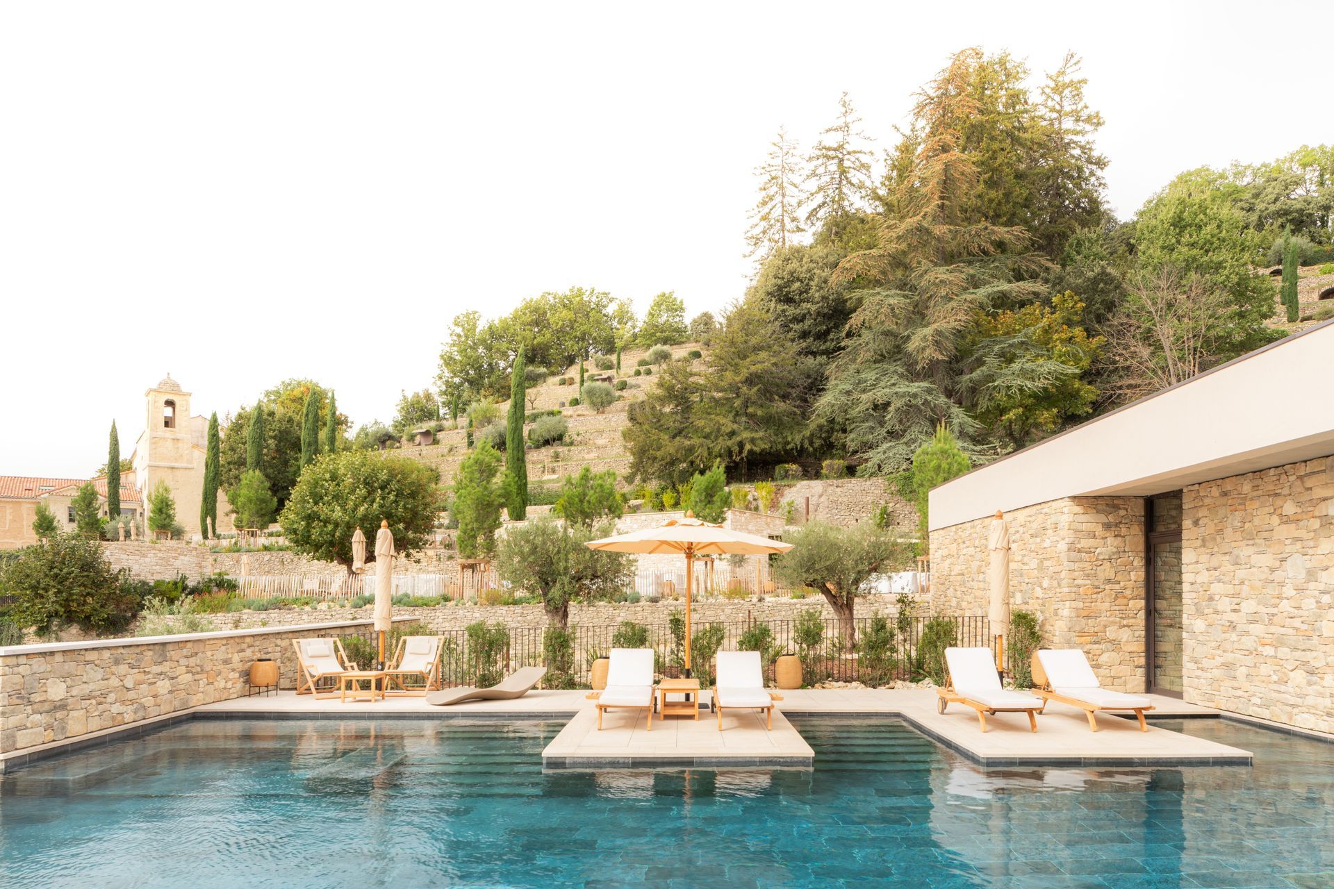 Une grande piscine entourée de chaises et de parasols devant un bâtiment en pierre.