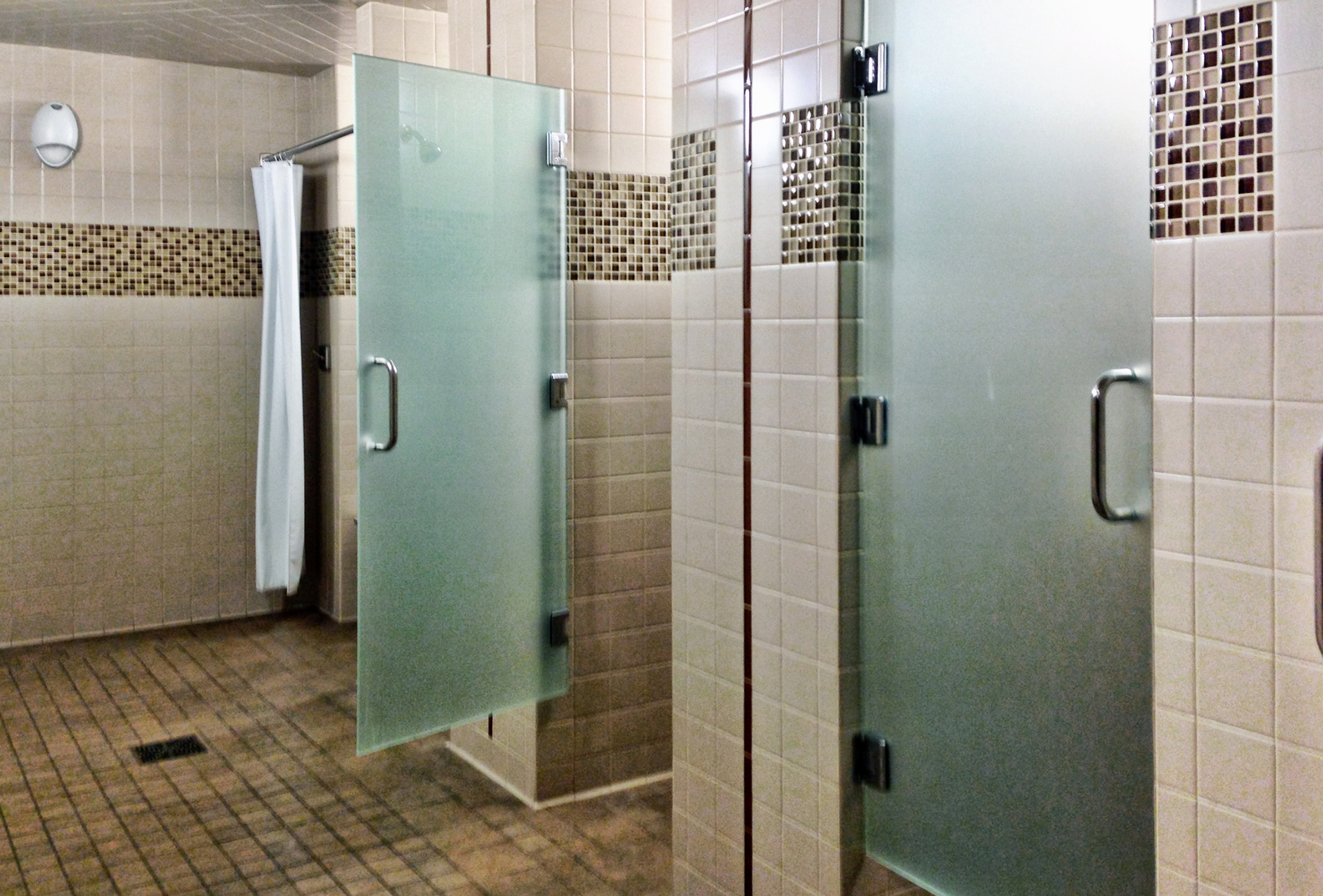 A bathroom with two shower stalls with frosted glass doors
