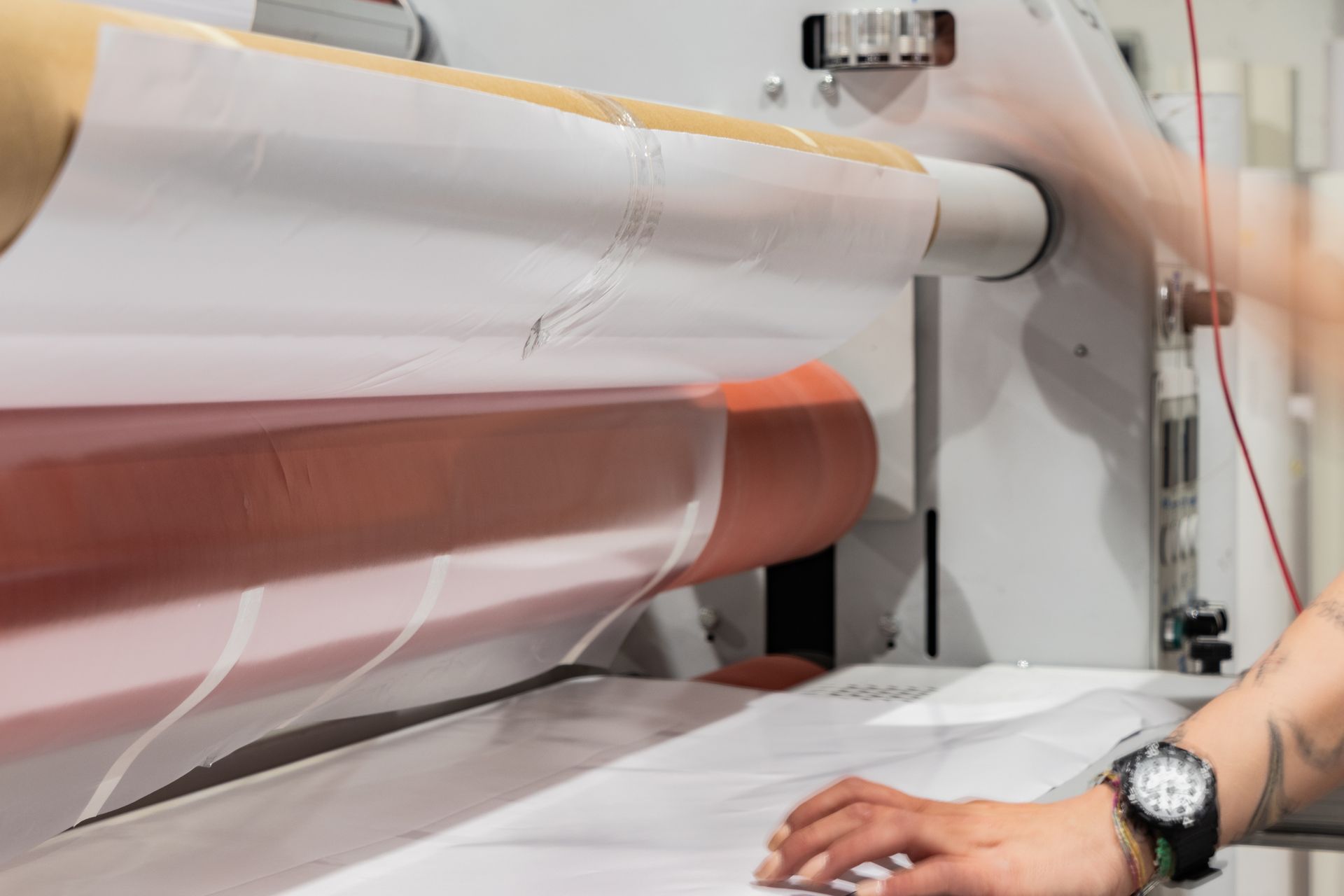 Person operating a laminating machine, white and red material, close-up.