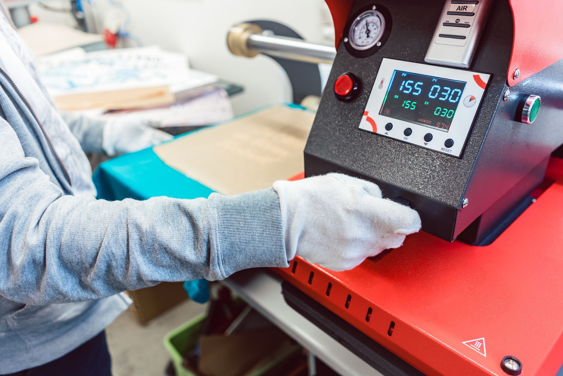 Person using heat press machine with digital display and safety gloves.