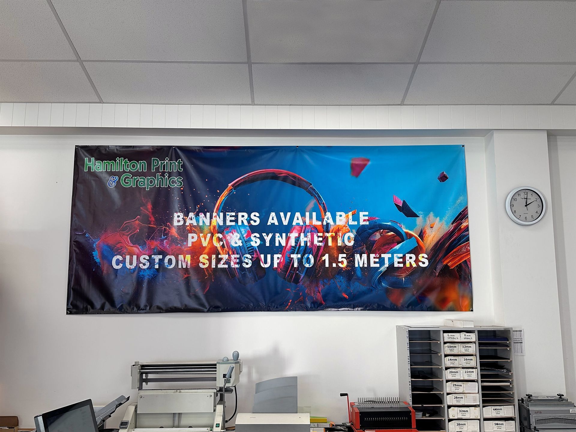 Banner advertising PVC & synthetic banners, custom sizes up to 1.5 meters, hung in a workshop with equipment.