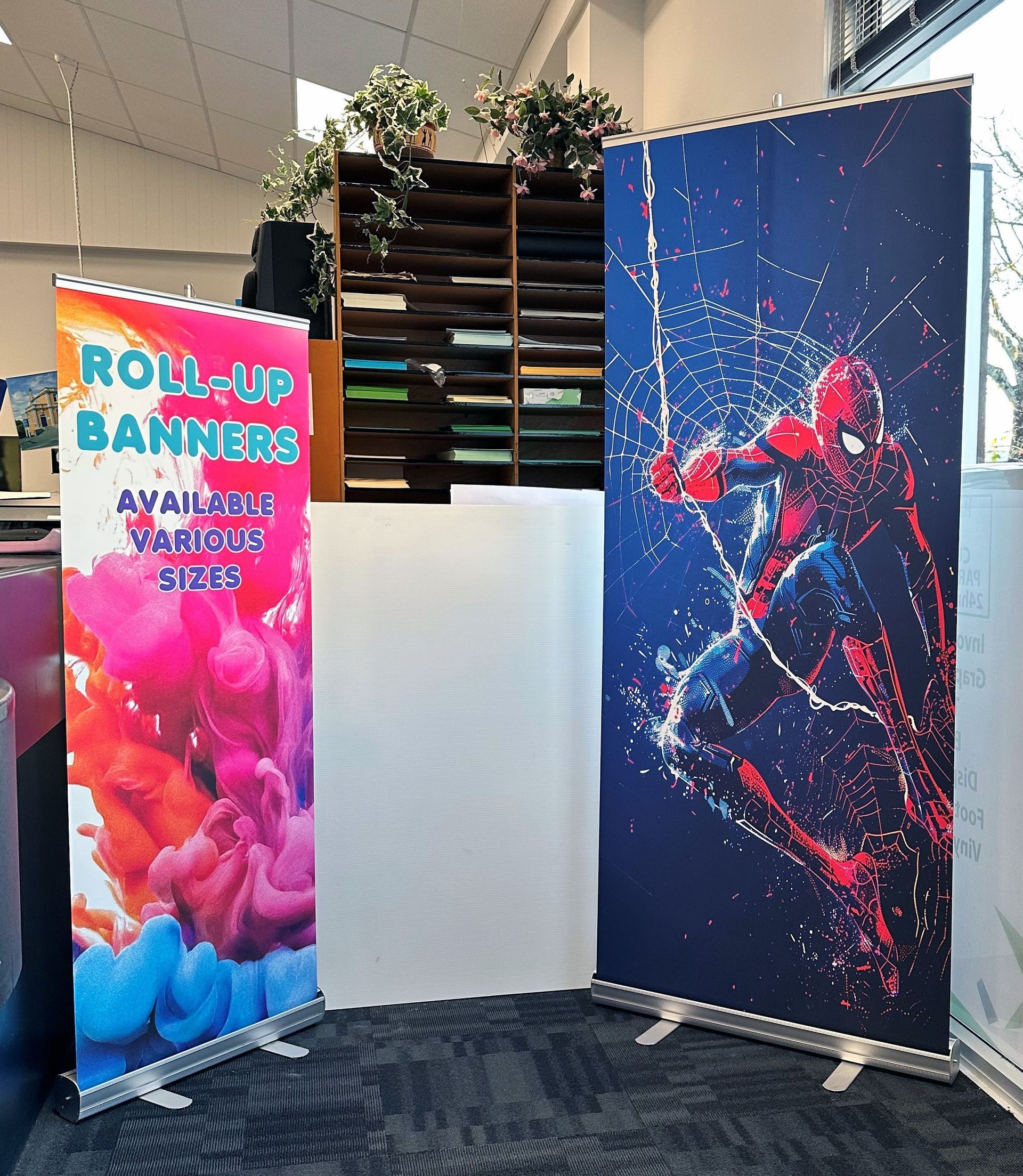 Roll-up banners in an office. One has colorful ink, the other Spiderman.