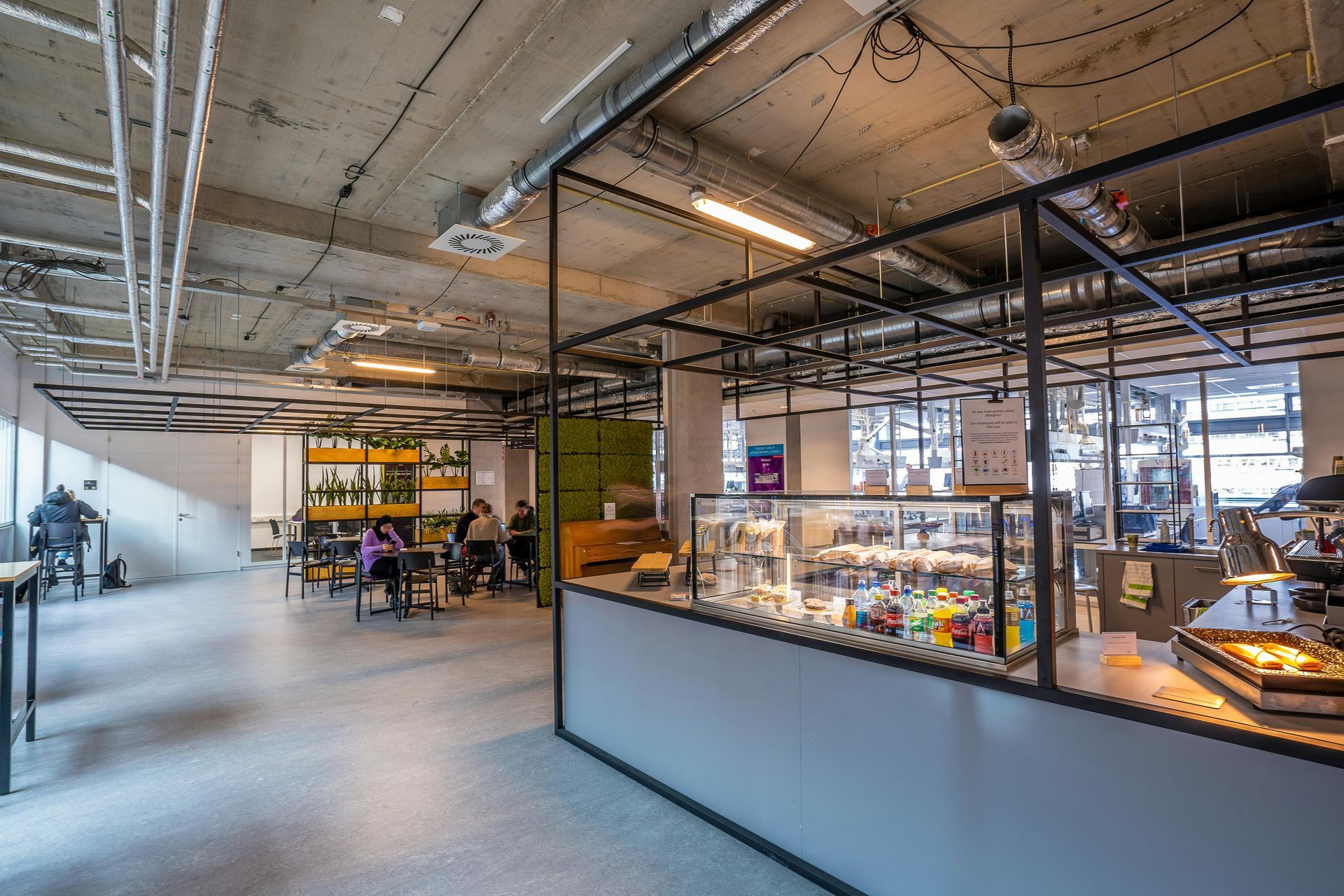 A spacious modern cafeteria with industrial design, showcasing people dining and working in a relaxe