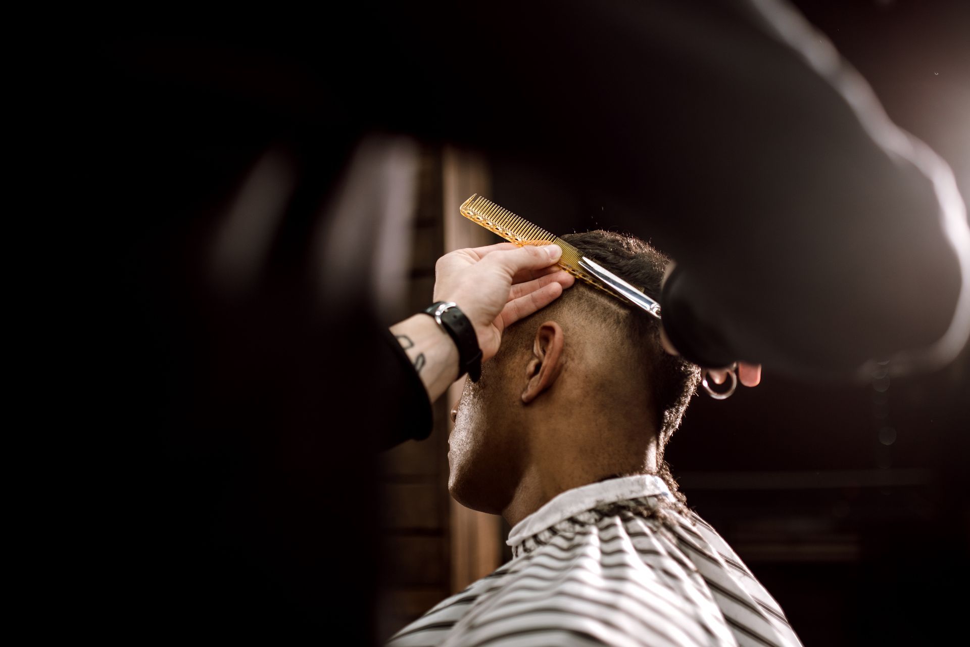 Barber trimming a client's hair with clippers in a dimly lit barbershop