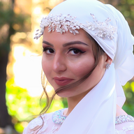 A woman wearing a white turban and a white dress is looking at the camera.