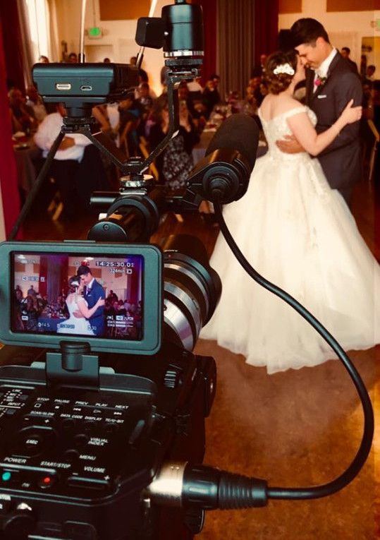 A bride and groom are dancing in front of a camera