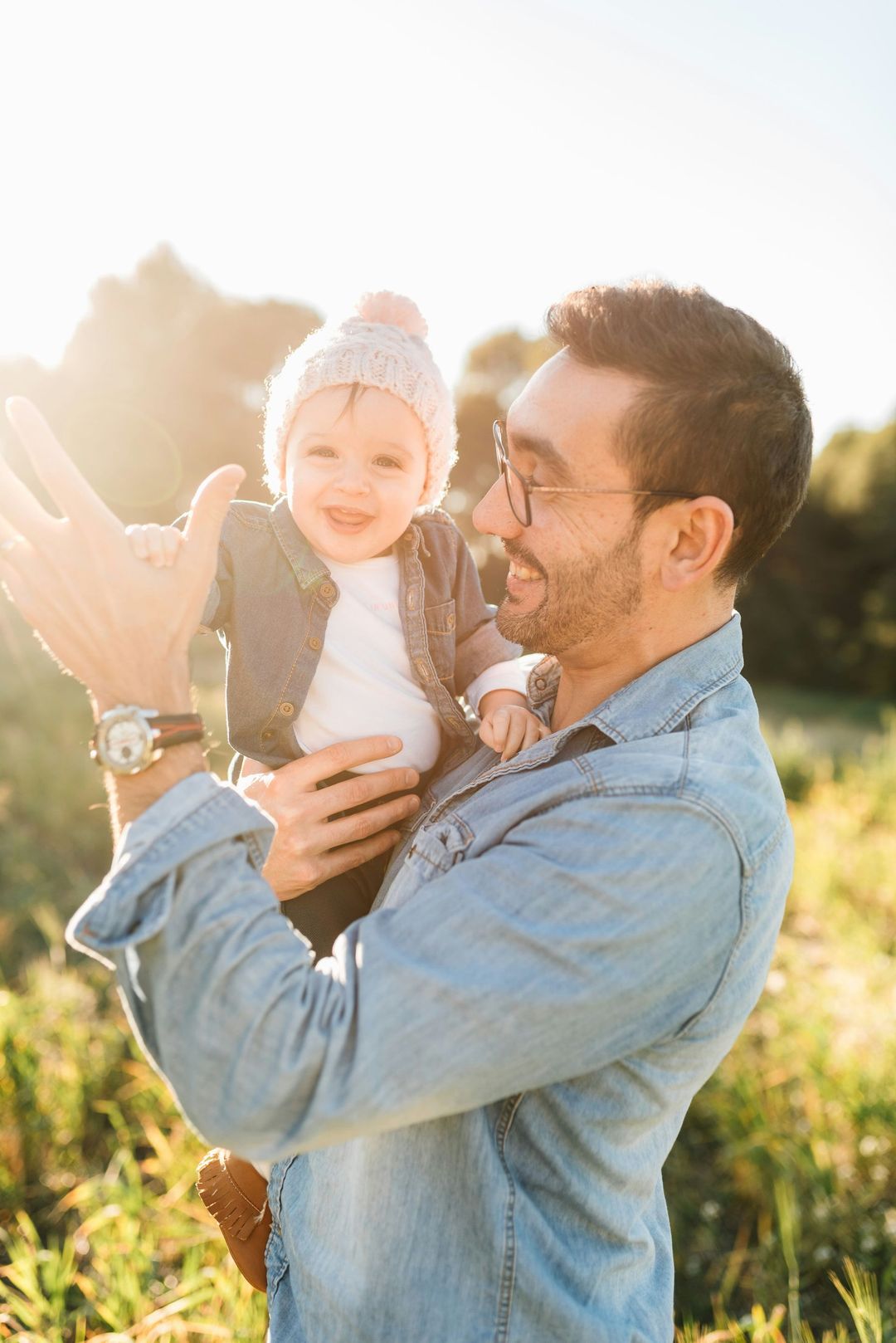 A man is holding a baby in his arms in a field.