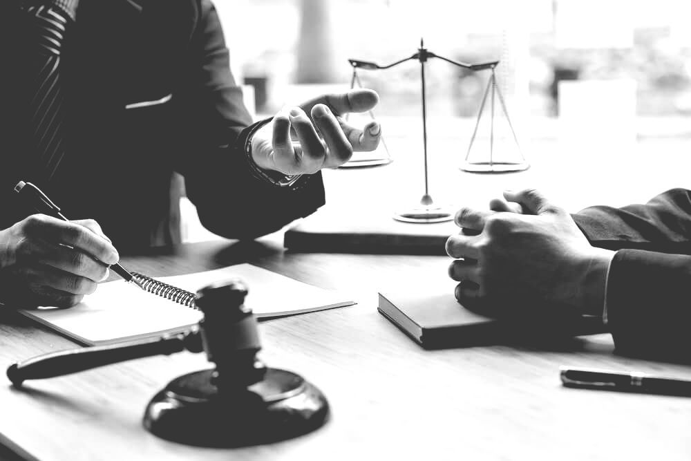 Two Men Sit At A Table With A Gavel And Scales Of Justice — Farrell Lusher Solicitors In Wagga Wagga, NSW