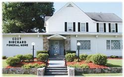 The front of a white funeral home with stairs leading up to it.