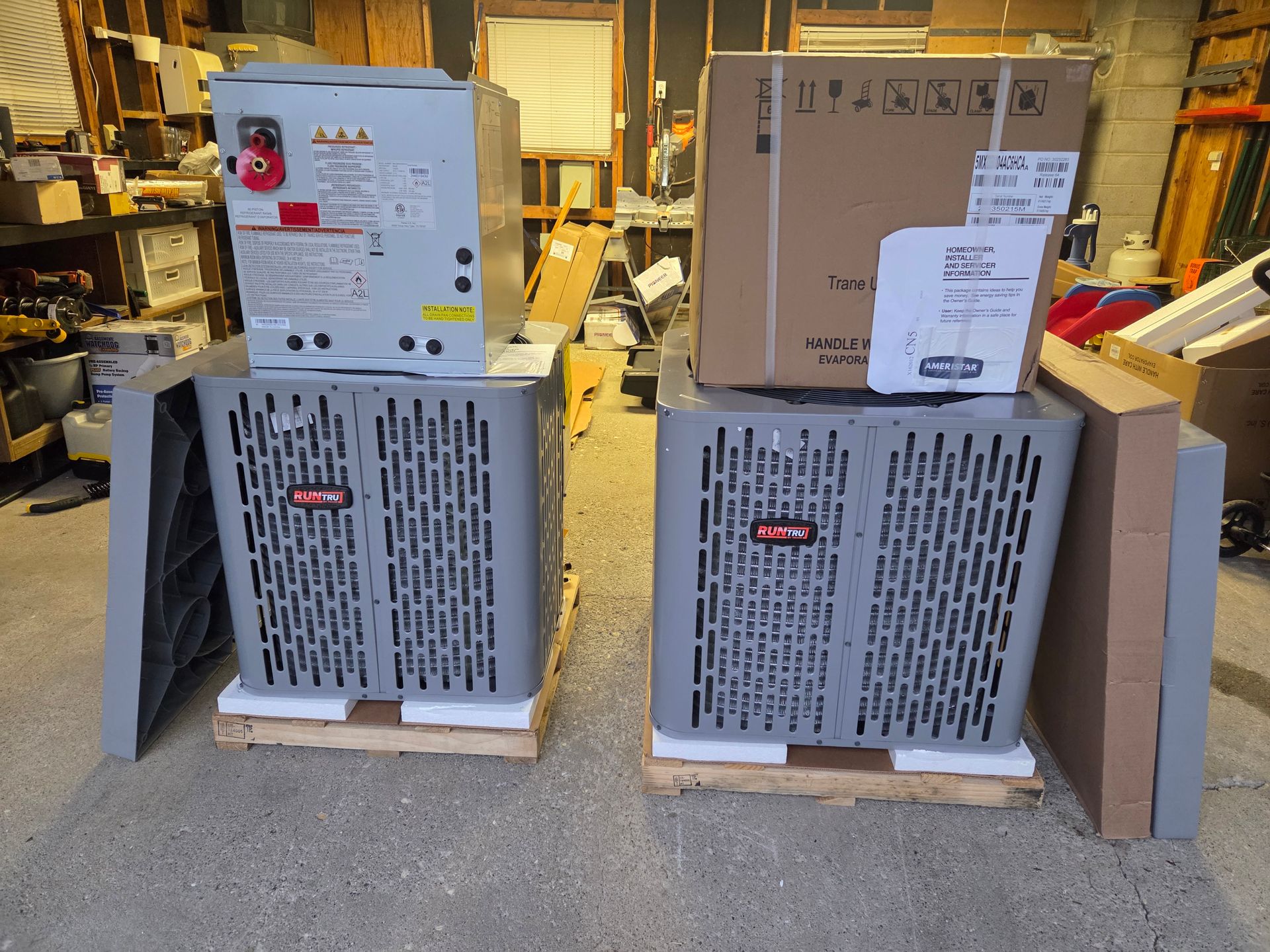 Two gray air conditioning units, boxes, and a control unit on pallets in a warehouse setting.
