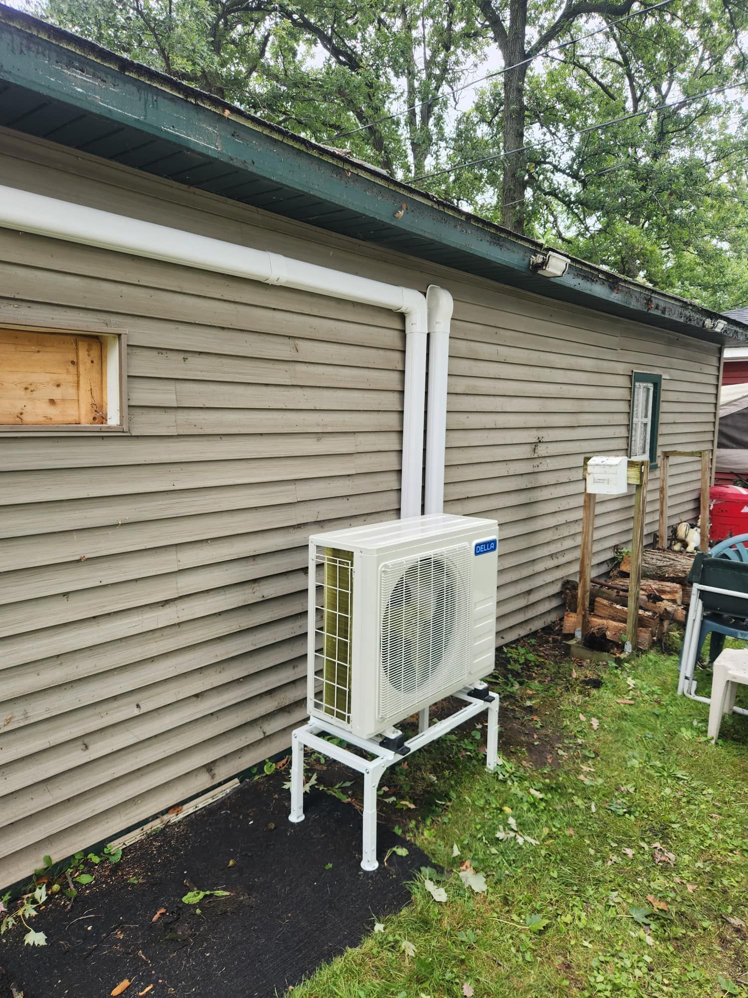Air conditioning unit on a white stand outside a building with white pipes.