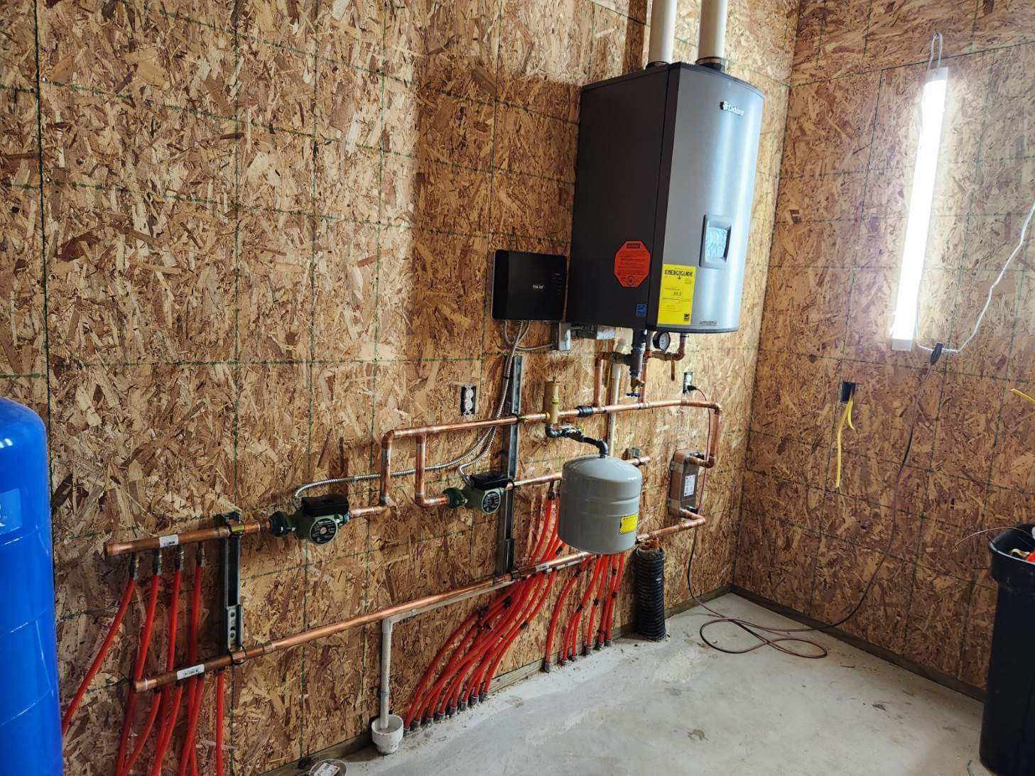 Water heater and piping installed on a wood wall. Copper pipes and orange tubing are visible.