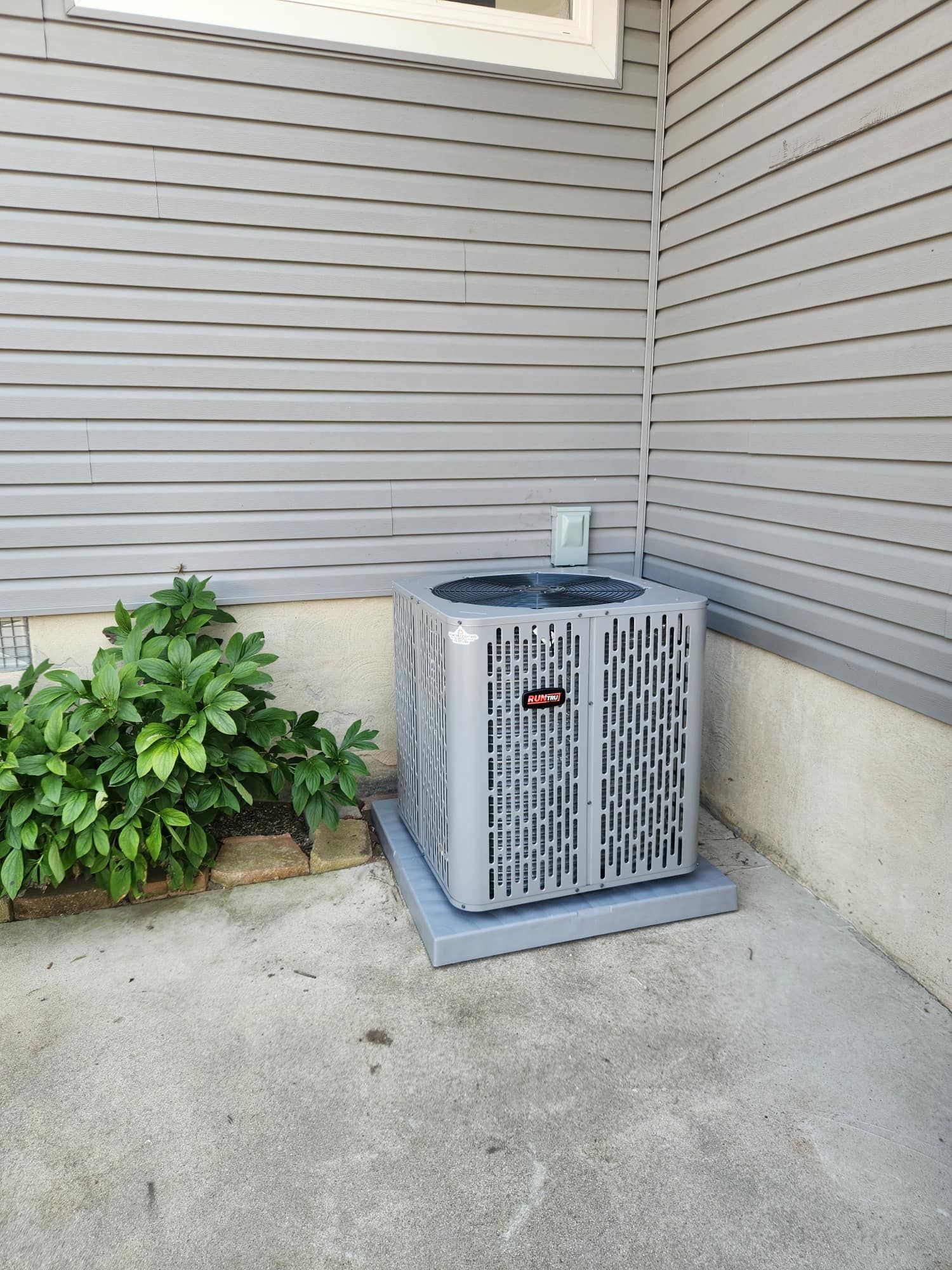 Gray air conditioning unit on a concrete pad near a house with gray siding.