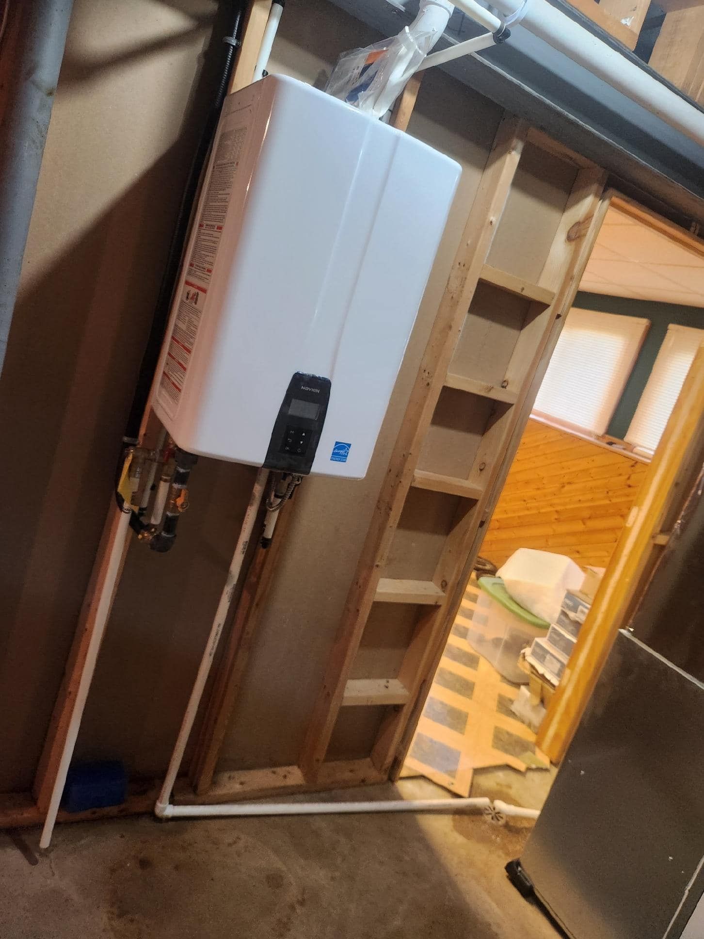 White tankless water heater mounted on wooden studs in a basement.