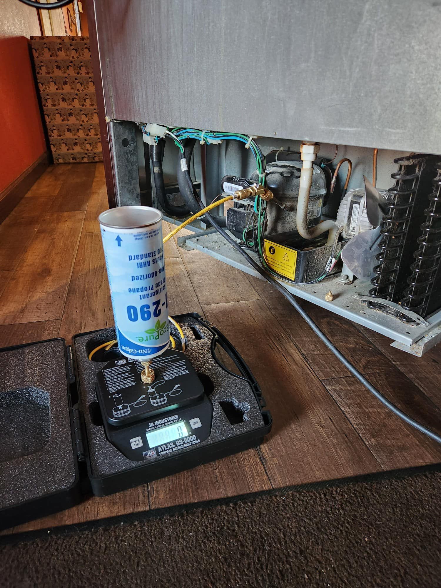 Refrigerator being charged with refrigerant; can on scale connected to unit.