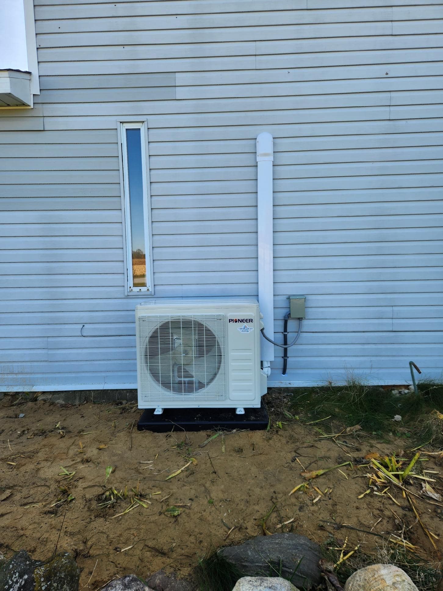 An outdoor AC unit installed on a side of a light blue house. White drainpipe runs up the wall.