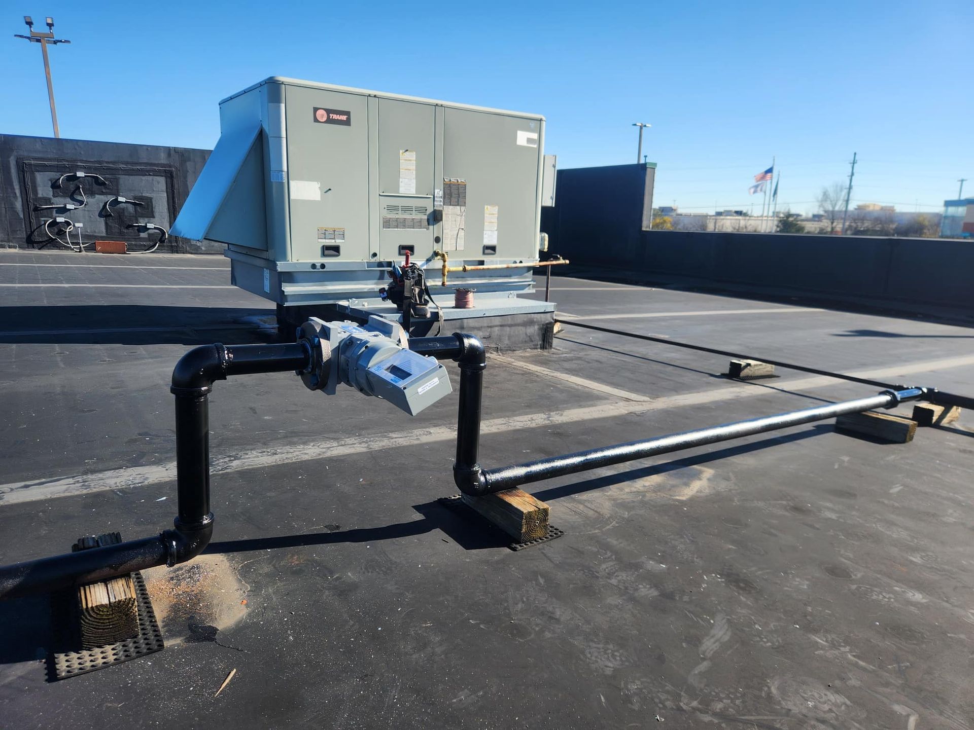 HVAC unit on a rooftop, with piping and supports. Blue sky backdrop.